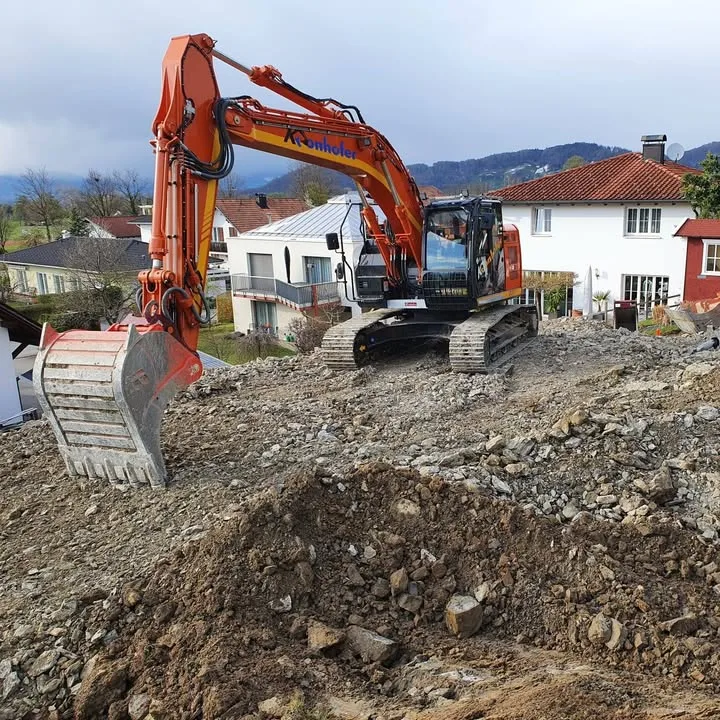 Oranger Kettenbagger mit Kronhofer-Beschriftung auf einer Aushubstelle zwischen Wohnhäusern